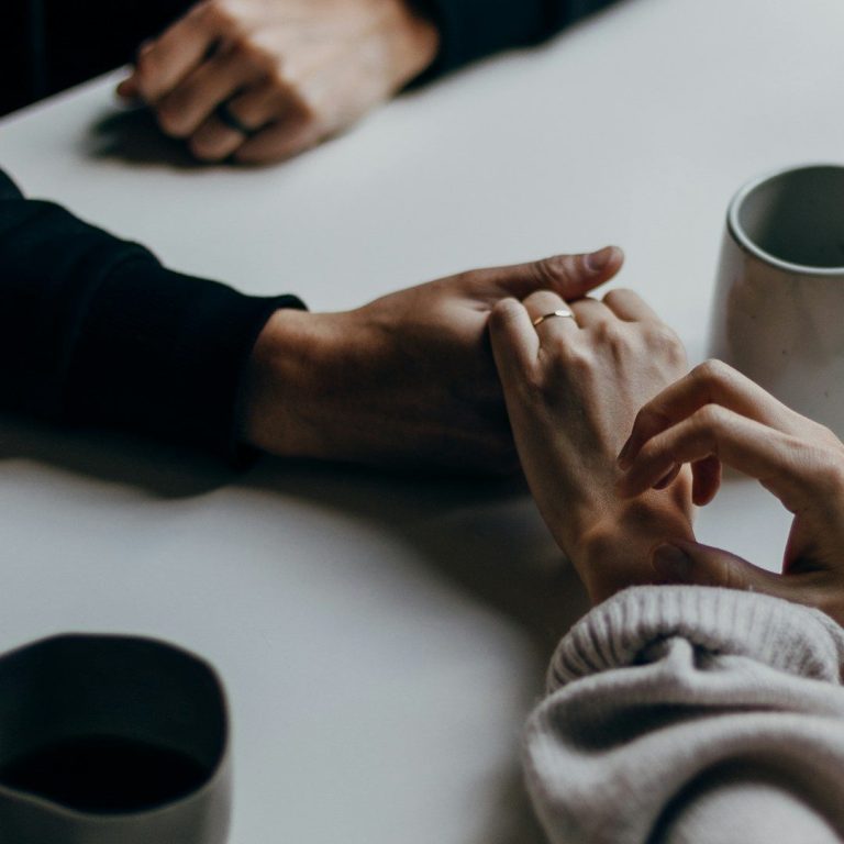 Zwei Hände greifen sich, umgeben von Kaffeetassen auf einem Tisch.